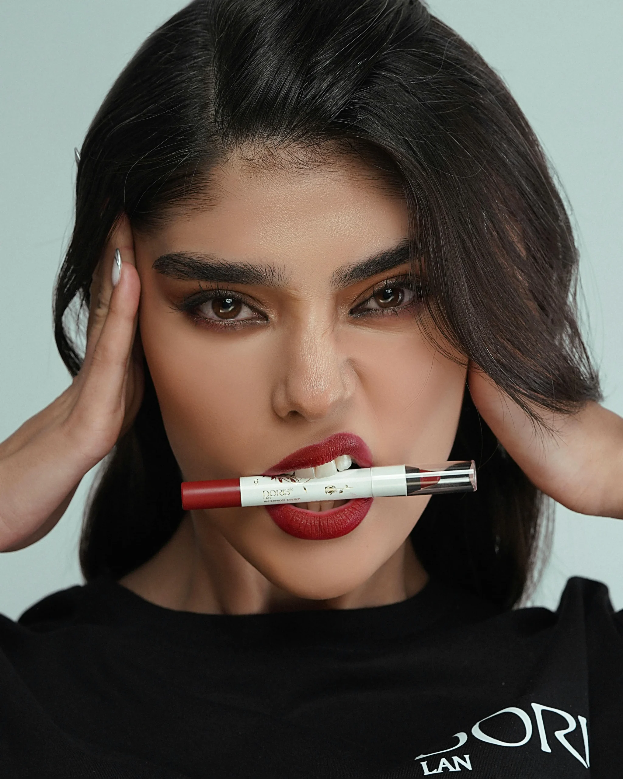 Mujer con labios maquillados en rojo intenso, sosteniendo un delineador de labios con los dientes. Look atrevido y elegante.